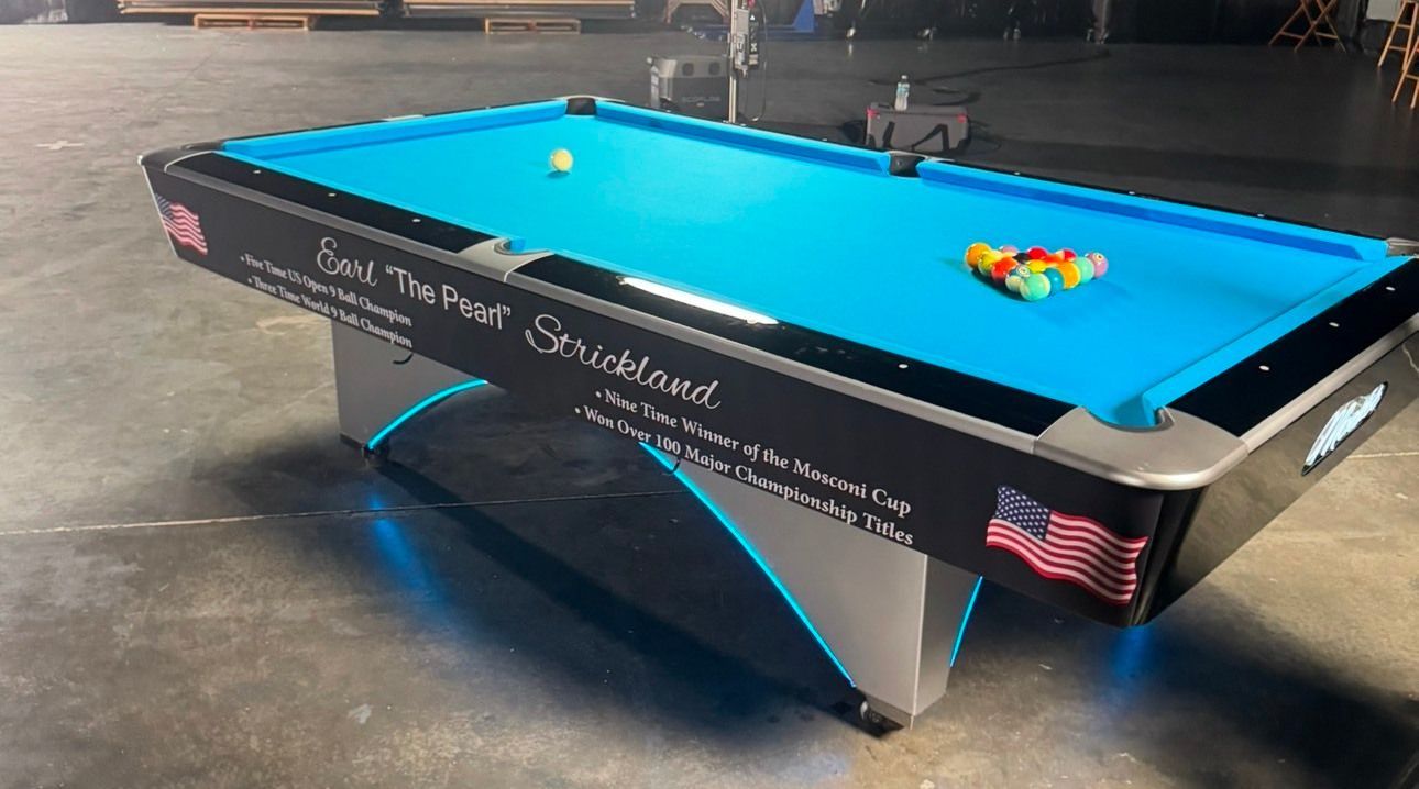 A pool table with a blue cloth is sitting on a concrete floor.