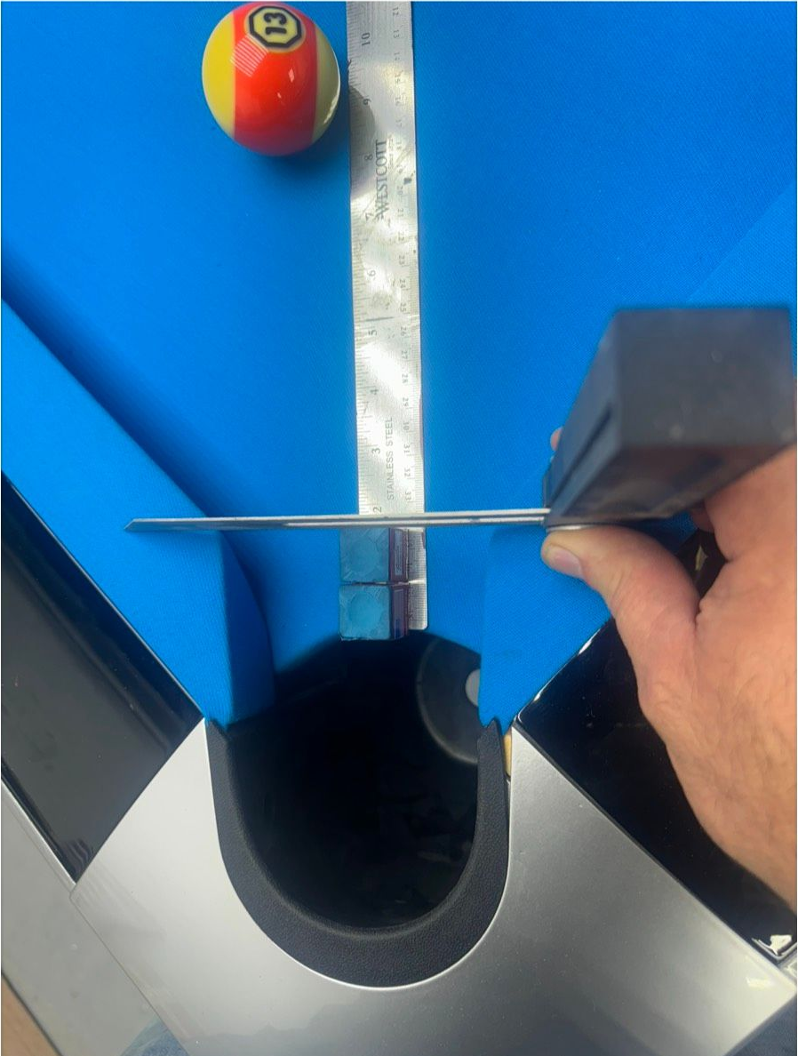 Pool table with the 13 ball and a player using a level near the corner pocket. Blue felt, silver rail.