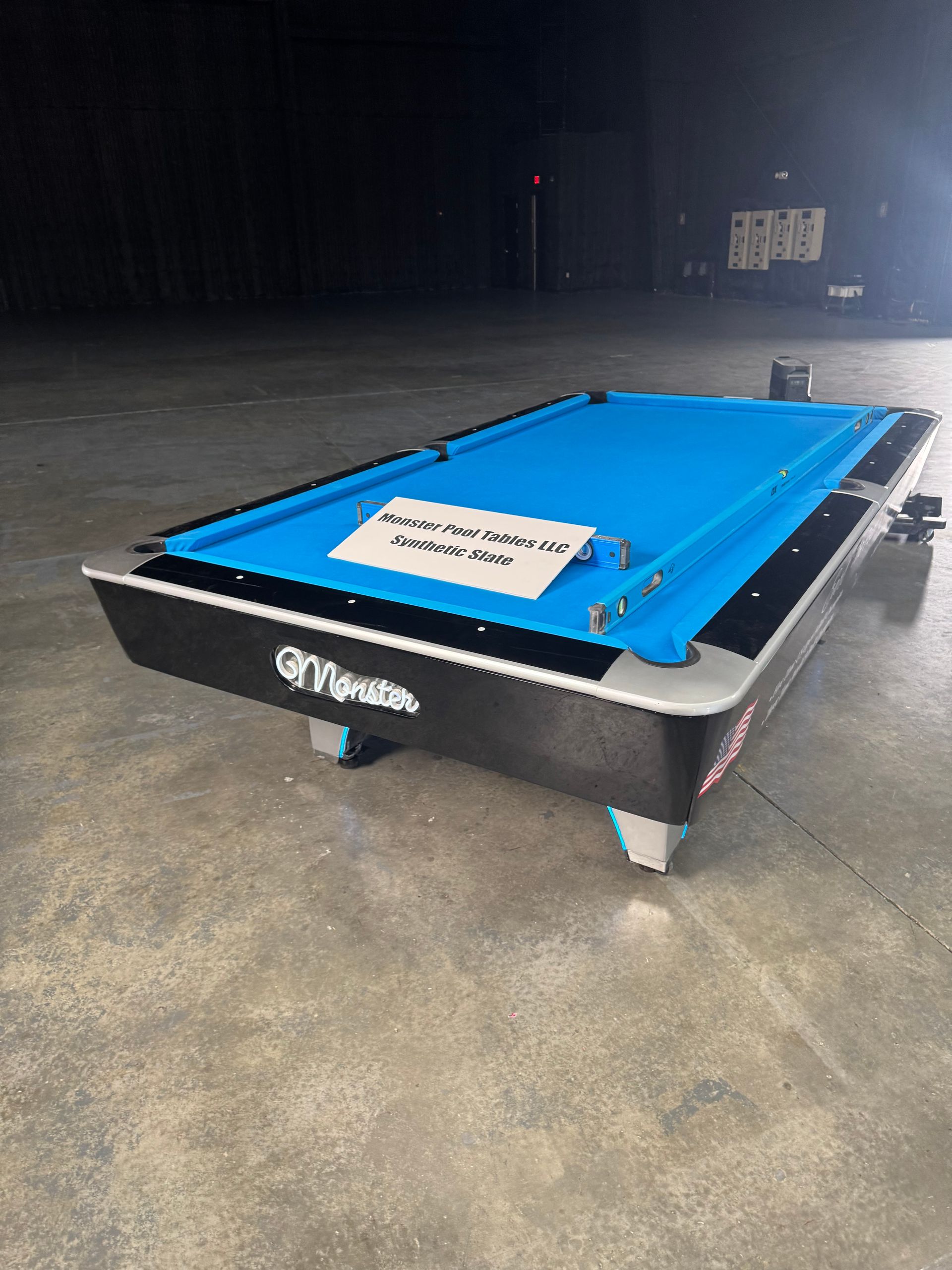 A pool table with a blue cloth is sitting on a concrete floor.