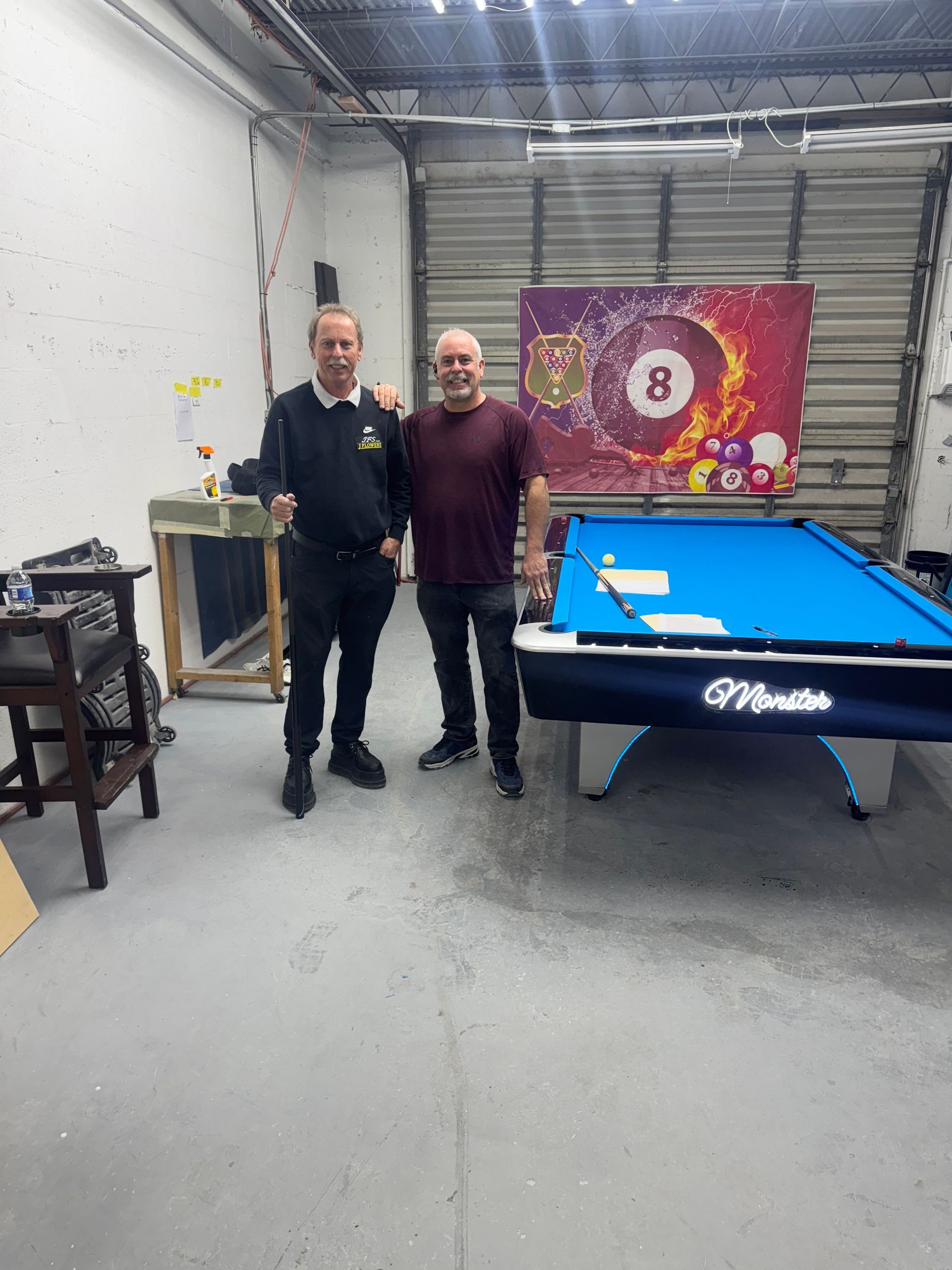 Two men standing in front of a pool table with the number 8 on it