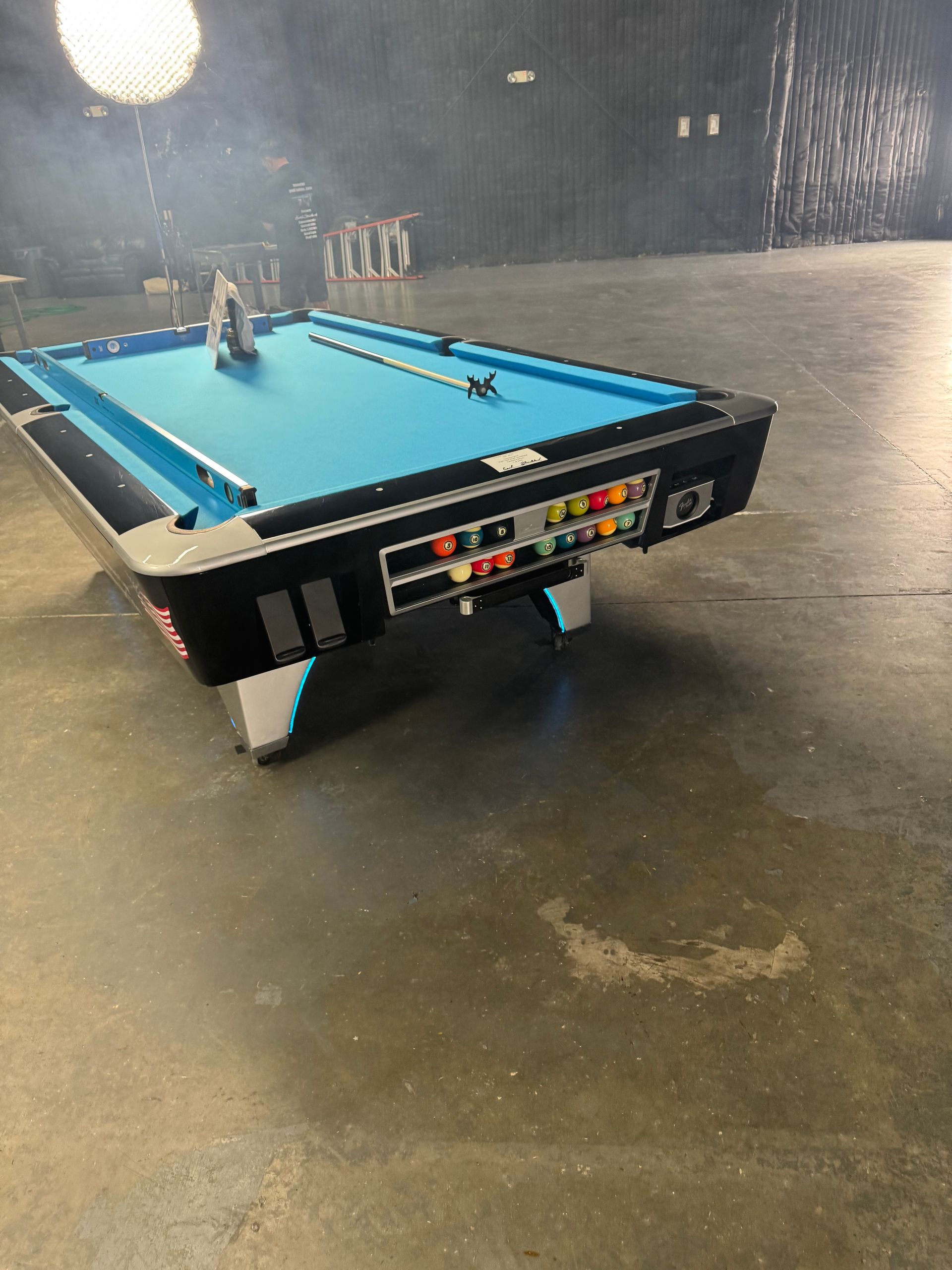 A pool table is sitting on a concrete floor in a dark room.