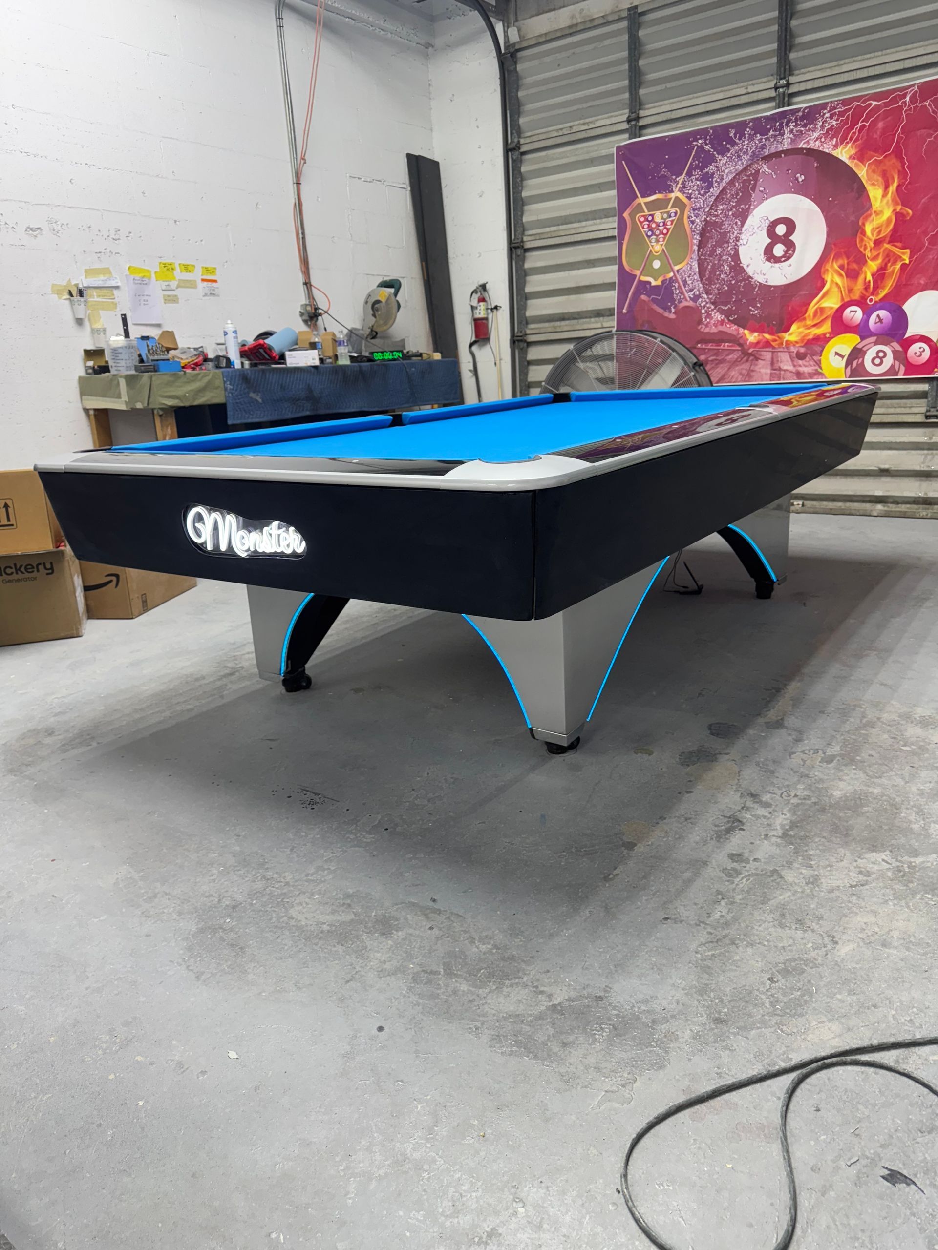 A pool table with a blue cloth and a pool cue in a room.