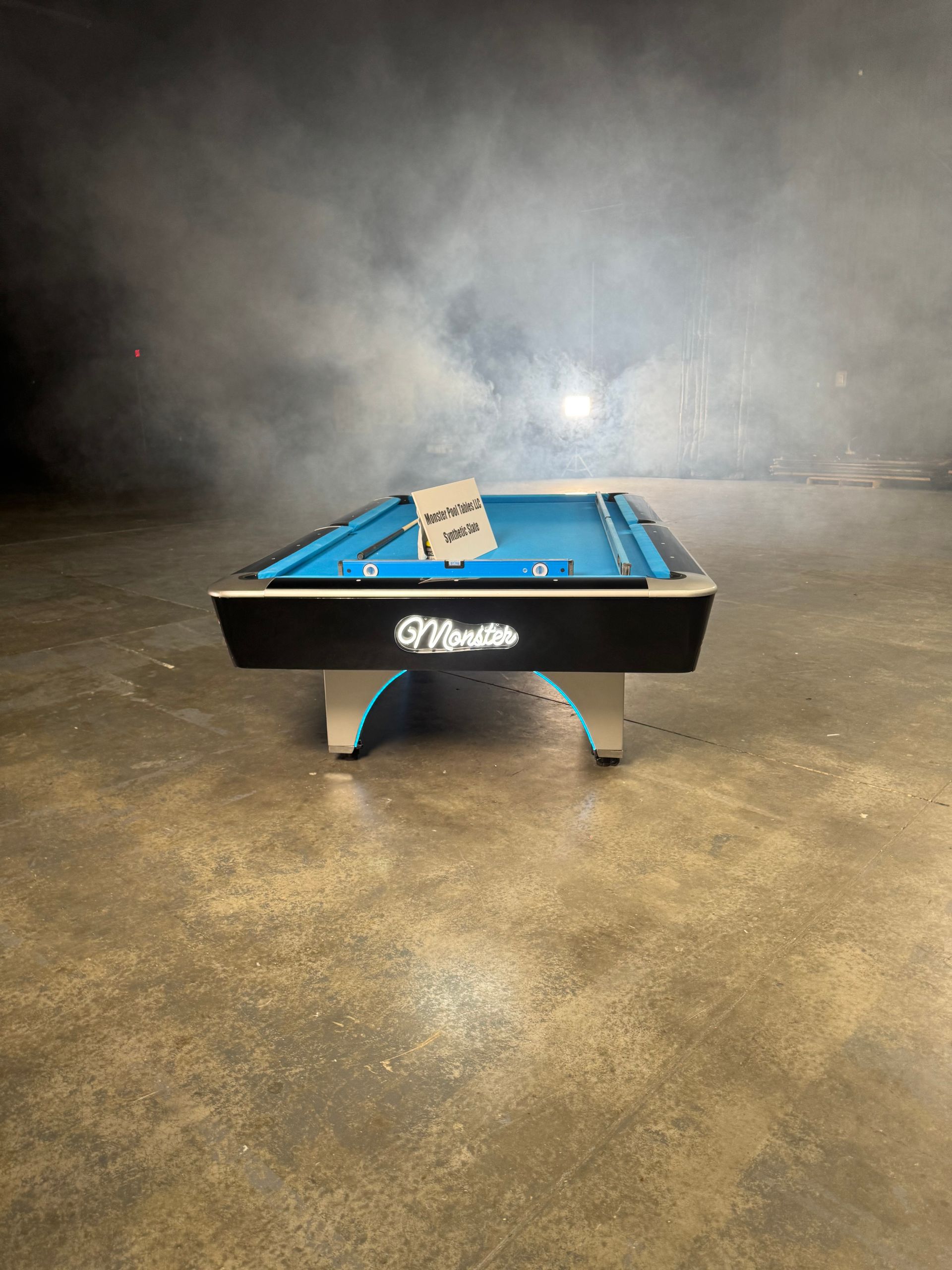 A pool table is sitting on a concrete floor in a dark room.