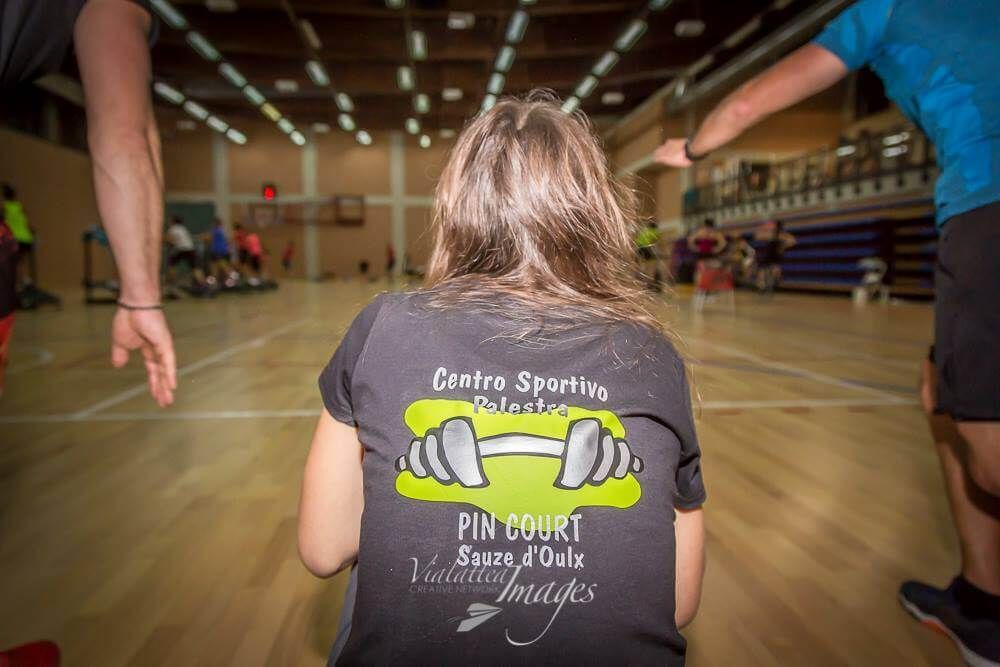 Una donna è seduta sul pavimento di una palestra e indossa una maglietta da baseball.