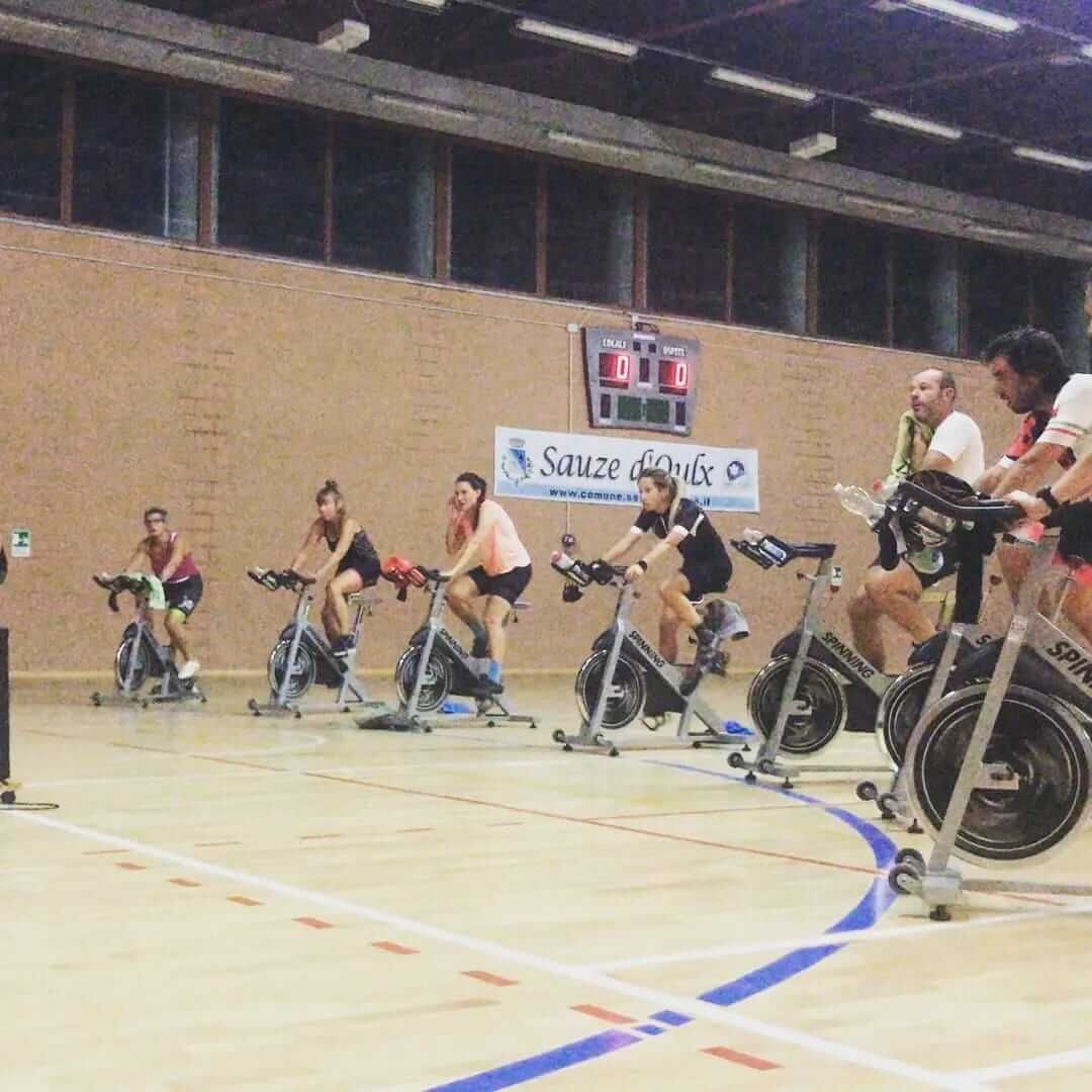 Un gruppo di persone sta pedalando su cyclette sul pavimento di una palestra