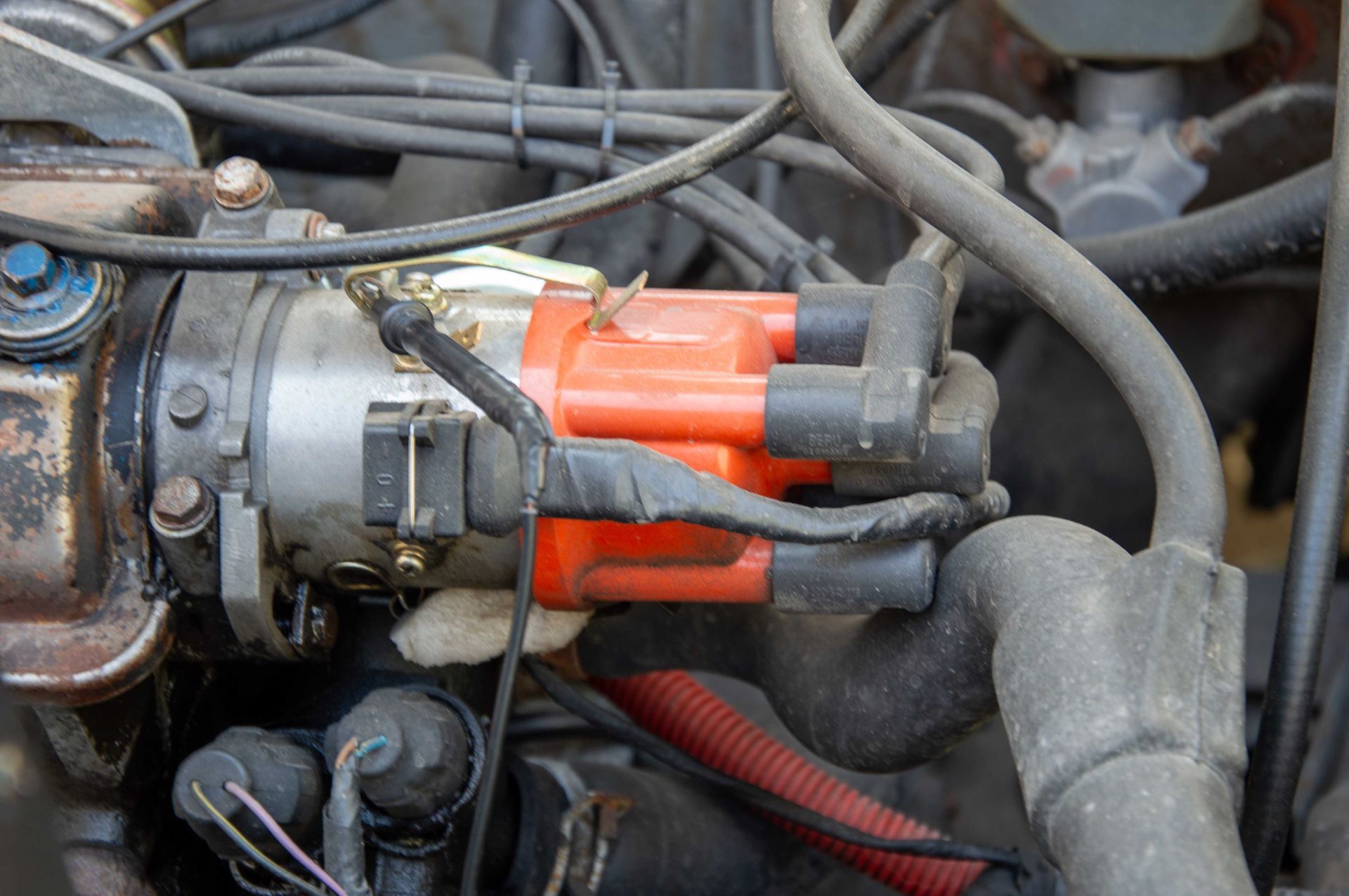 Gros plan sur un distributeur automobile orange avec des fils d'allumage noirs fixés à l'intérieur du compartiment moteur d'une voiture.