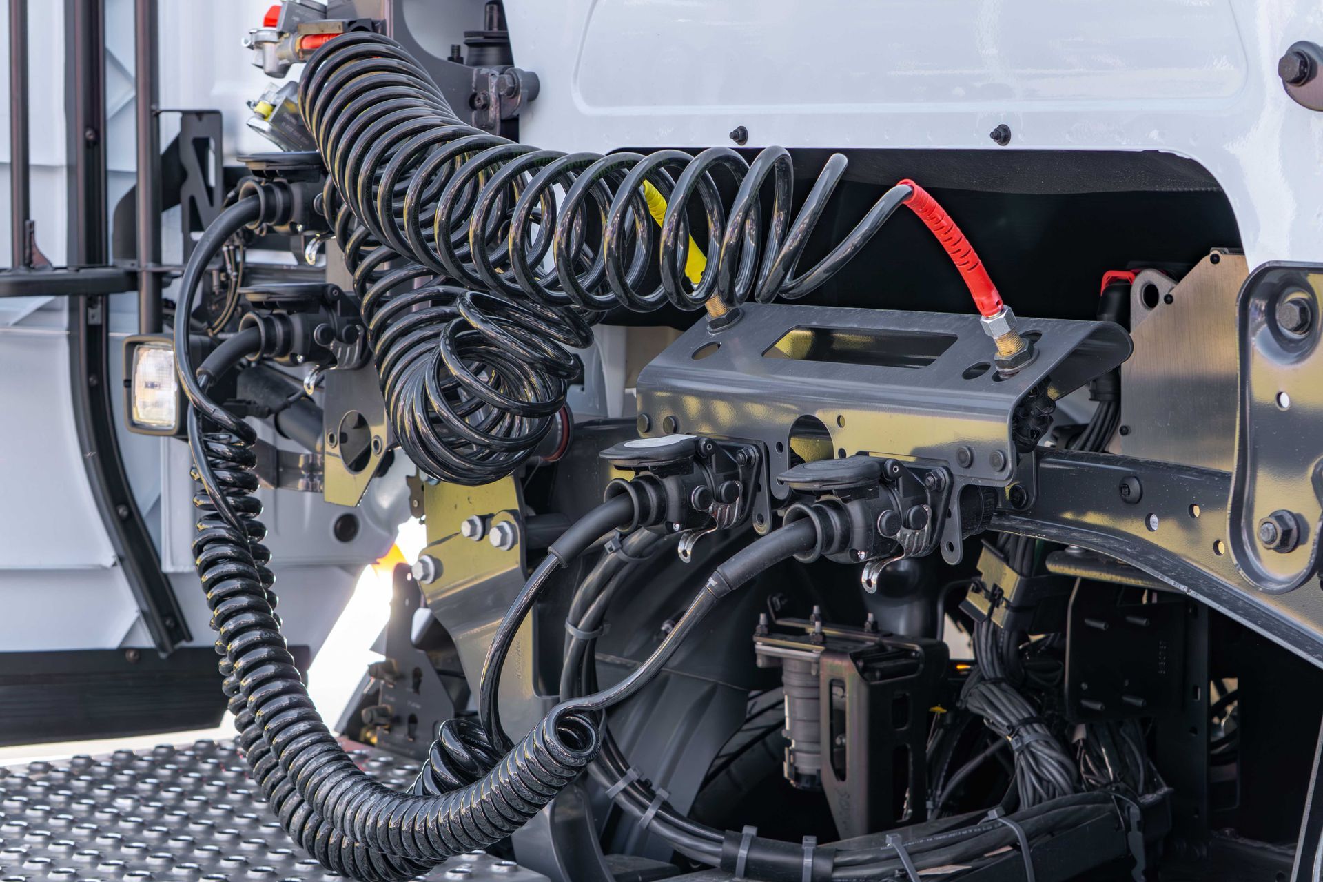 Coiled black air lines and an electrical cable connect the rear of a white semi-truck cab to its trailer connections.