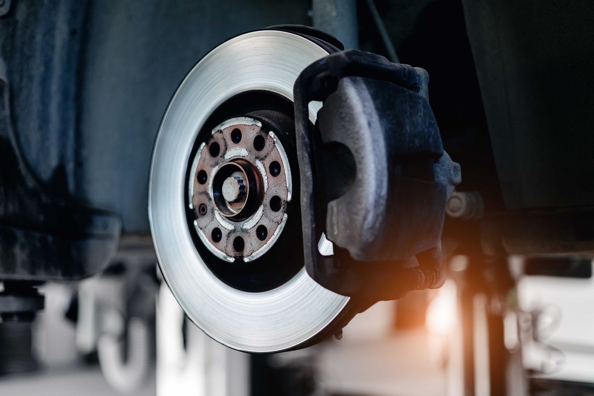 Disque et étrier de frein de voiture, vue rapprochée. Disque argenté, étrier noir, moyeu de roue visible, dessous du véhicule.