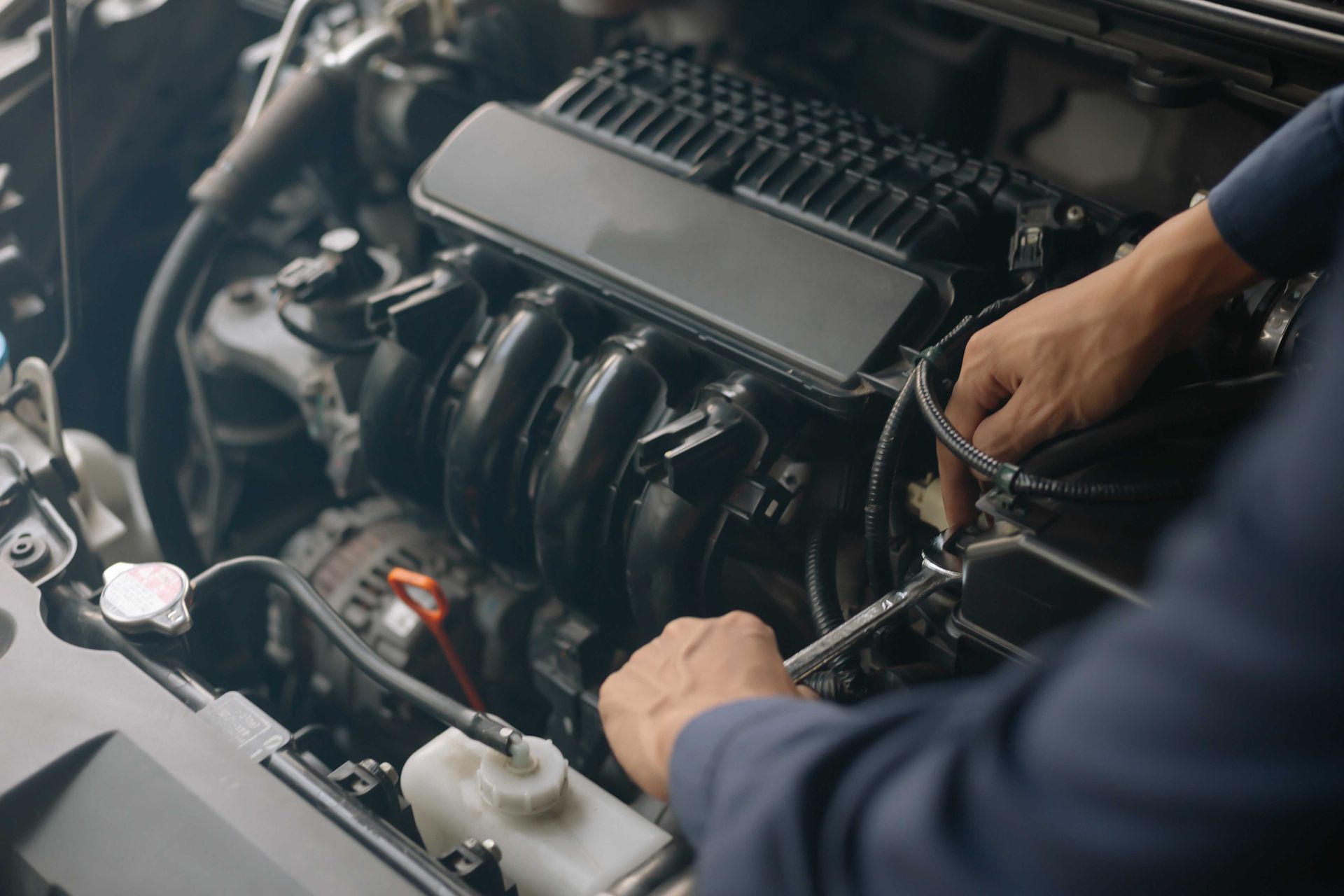 Un mécanicien travaille sur le moteur d'une voiture, ses mains sont visibles, dans un garage.