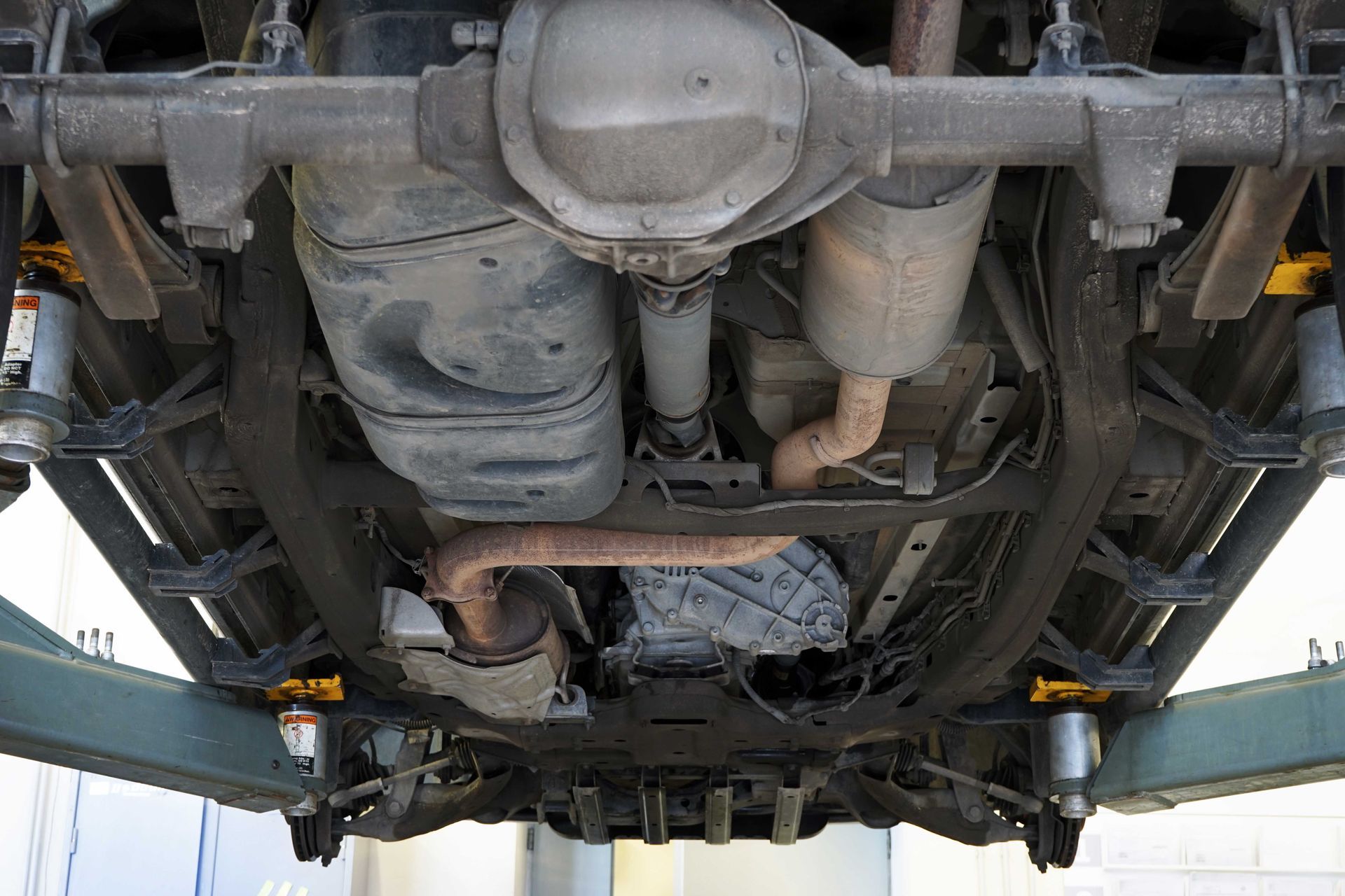 Vue de dessous d'un véhicule, montrant le châssis, le système d'échappement, le réservoir de carburant et les éléments de suspension.