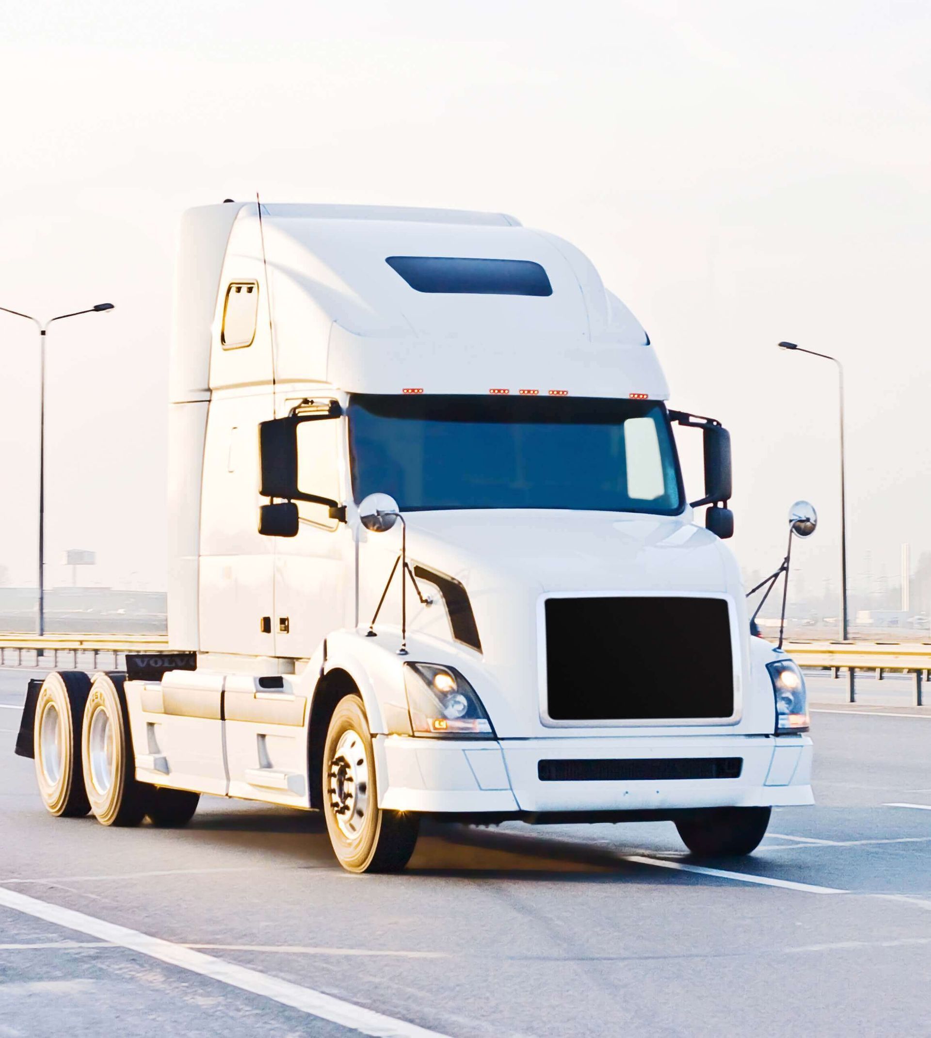 Un semi-remorque blanc sur un terrain goudronné, avec des lampadaires en arrière-plan.