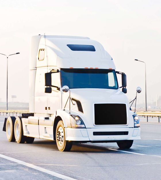 Un semi-remorque blanc sur un terrain goudronné, avec plusieurs lampadaires et un ciel brumeux en arrière-plan.