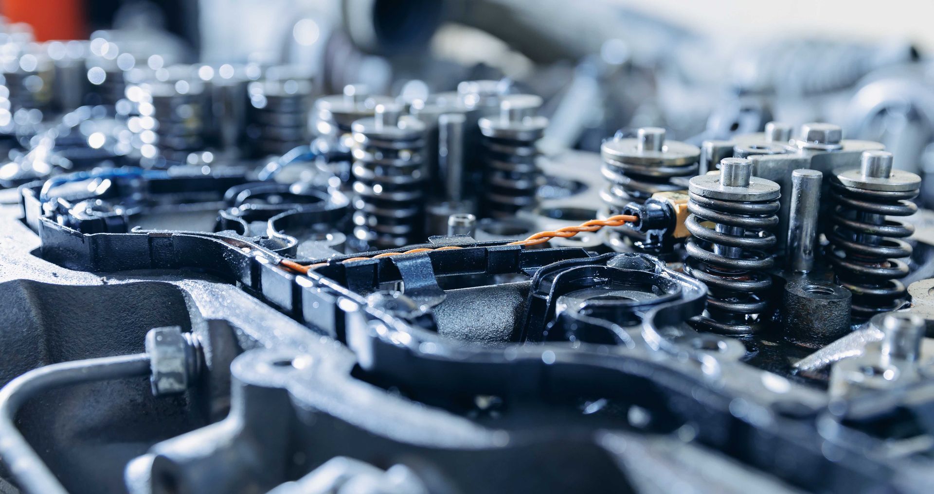 Gros plan sur des pièces du moteur, notamment des ressorts, des soupapes et une surface sombre et huileuse.