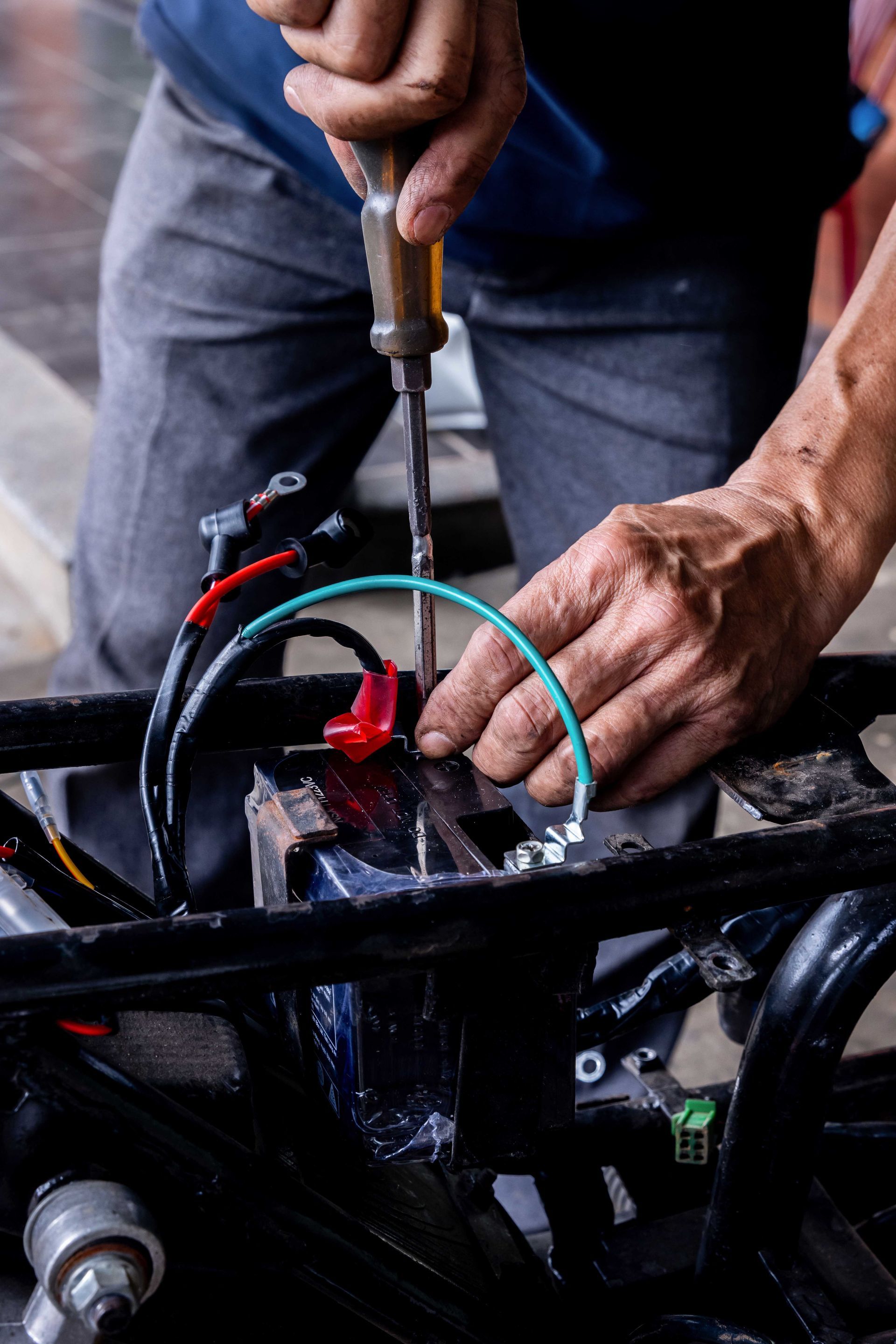 Une personne utilise un tournevis pour travailler sur une pièce mécanique noire, probablement une pièce de véhicule.
