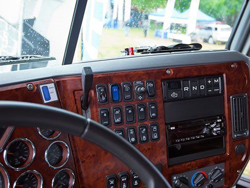 Tableau de bord d'un camion avec garnitures en imitation bois, boutons, cadrans et volant visibles.