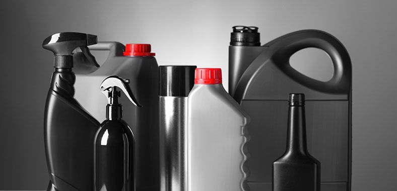 Assortiment de bouteilles et de récipients en plastique noir, certains avec des bouchons rouges, sur fond gris.