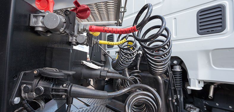 Gros plan sur le système de freinage pneumatique et les connexions électriques d'un semi-remorque, montrant les tuyaux enroulés et les lignes colorées.
