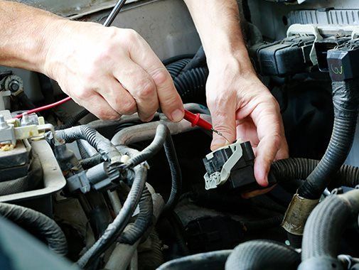 Des mains utilisent une sonde pour tester un composant du moteur d'une voiture.