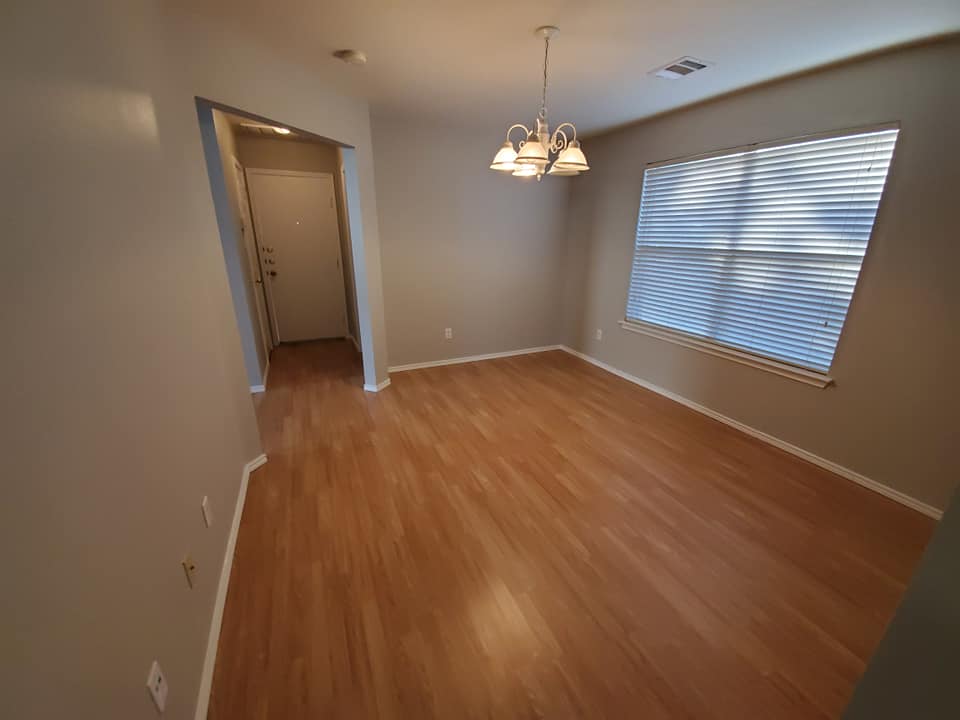 An empty dining room with hardwood floors and a chandelier hanging from the ceiling.