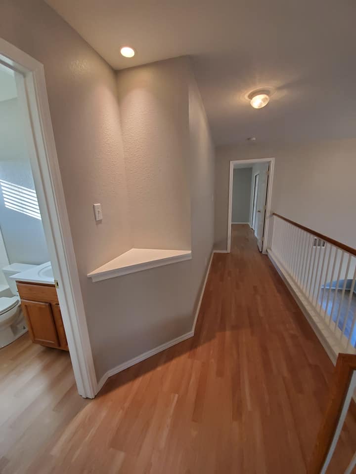 A long hallway with hardwood floors leading to a bathroom and stairs.