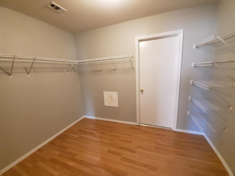 An empty walk in closet with hardwood floors and a white door.