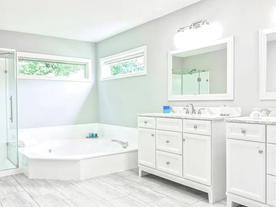 Bright white bathroom with soaking tub, double vanity, large mirror, and frosted windows.