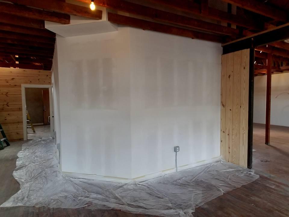 A room with white walls and wooden beams is being painted.