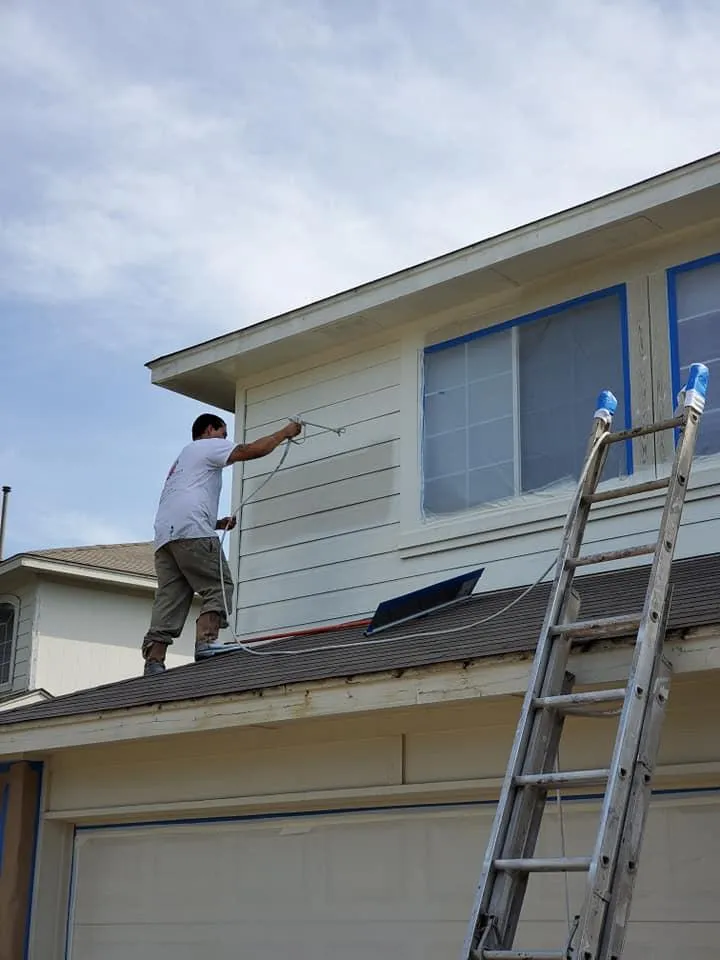 A man is standing on the roof of a house painting it.