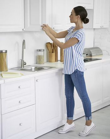 Woman in a striped shirt and jeans reaching into a white kitchen cabinet.