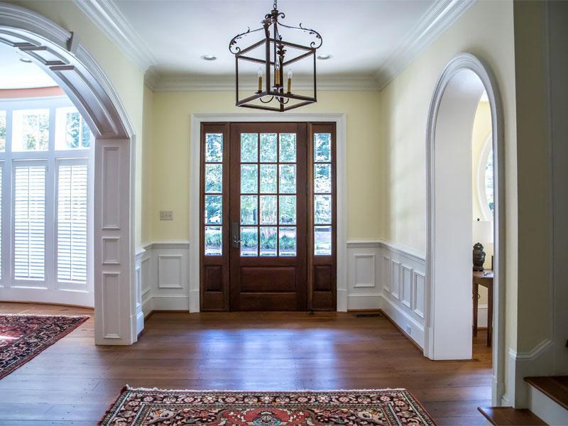 An empty hallway with a wooden door and a chandelier hanging from the ceiling.