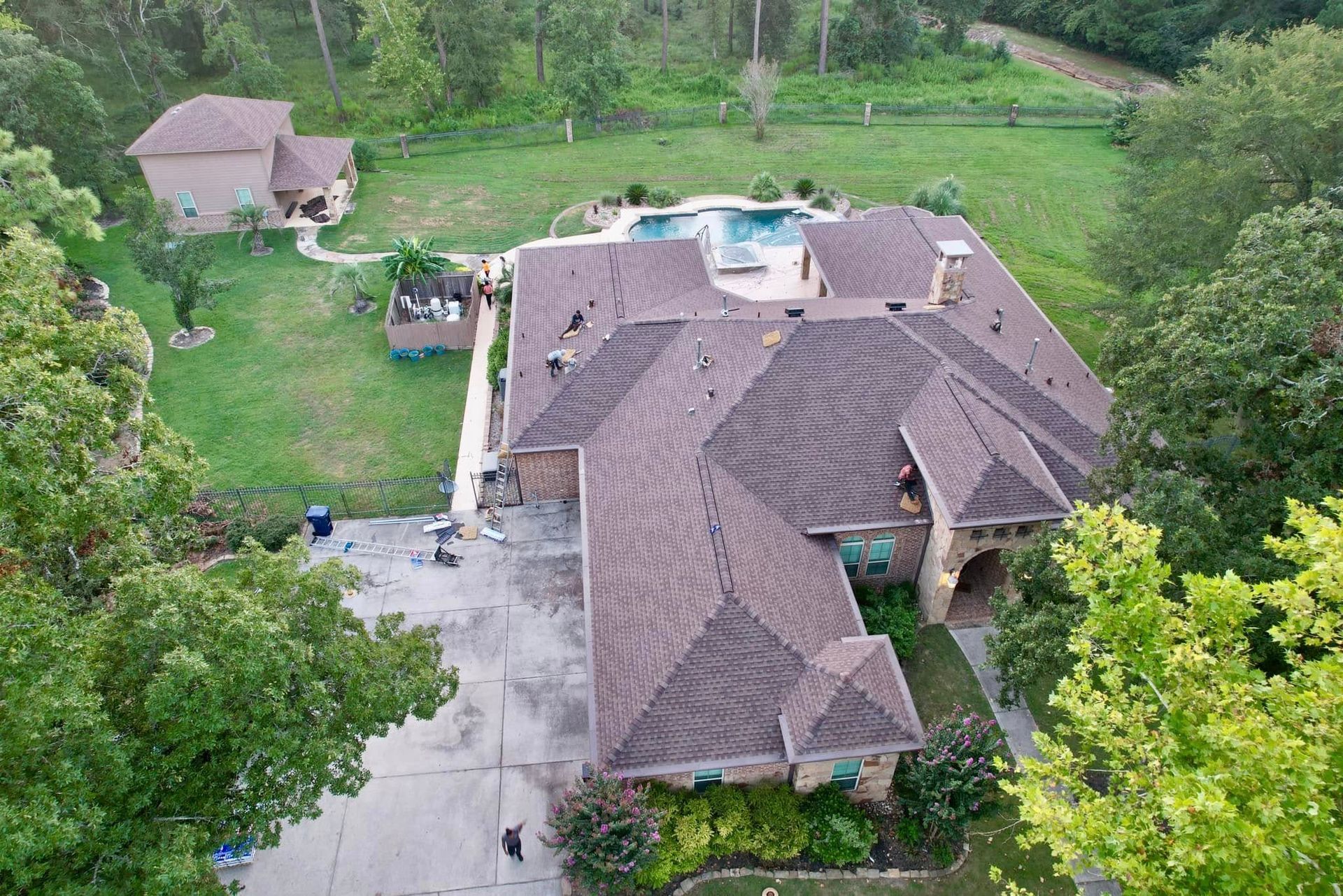 Aerial view of a large residential property featuring a sprawling brown roof, a pool, and a smaller detached building.