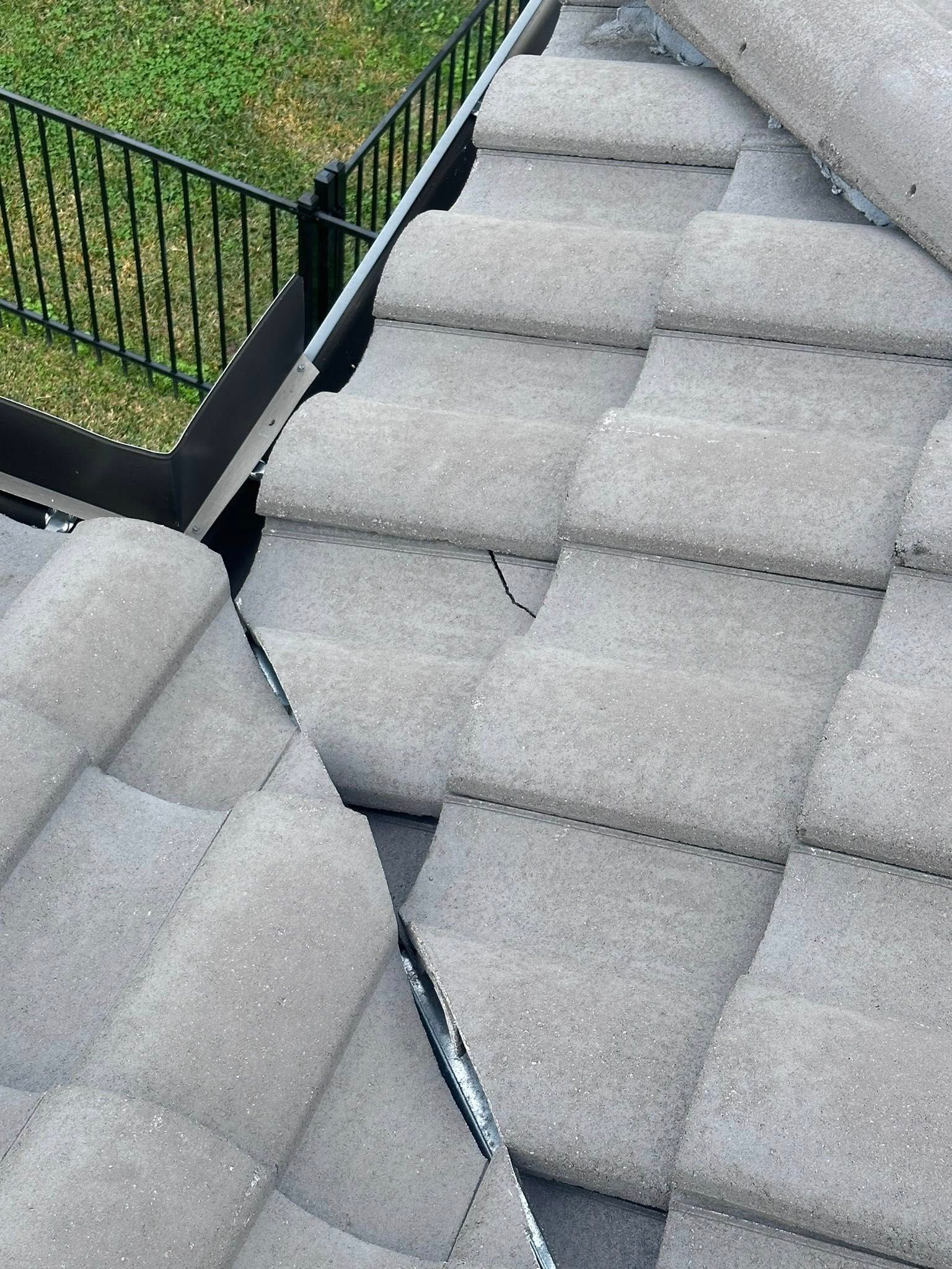 Close-up view of grey roof tiles installed on a slope, showing the overlap and a section of black flashing.