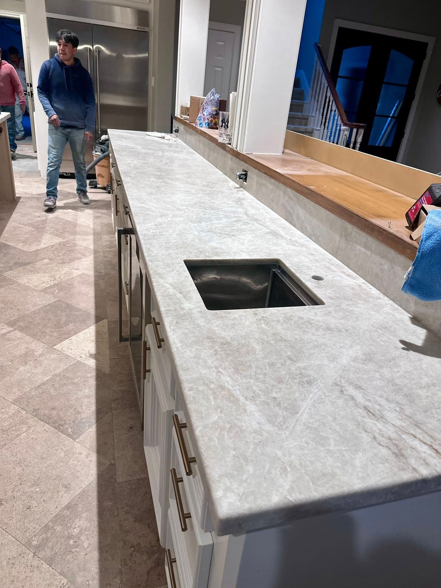A long, light-gray granite countertop with a square sink installed in a bright, modern kitchen with tiled floors.