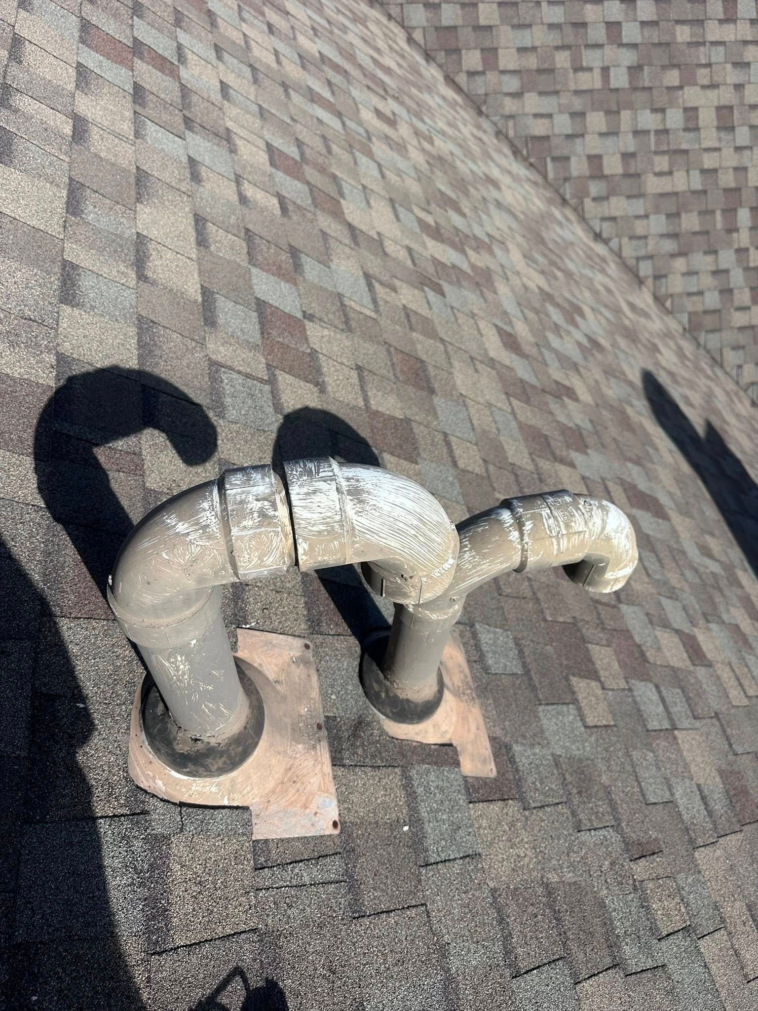 Two grey, curved plumbing vent pipes installed on a shingled residential roof.
