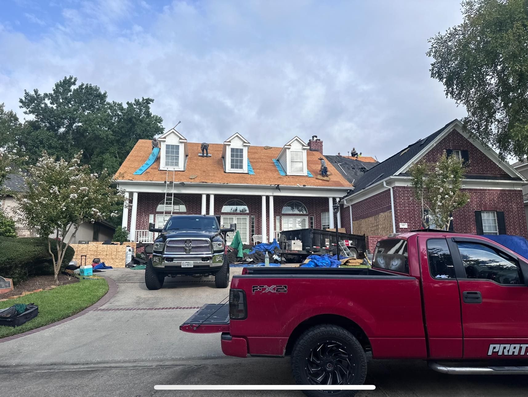 A red pickup truck is parked in a driveway in front of a house currently undergoing roof renovations.
