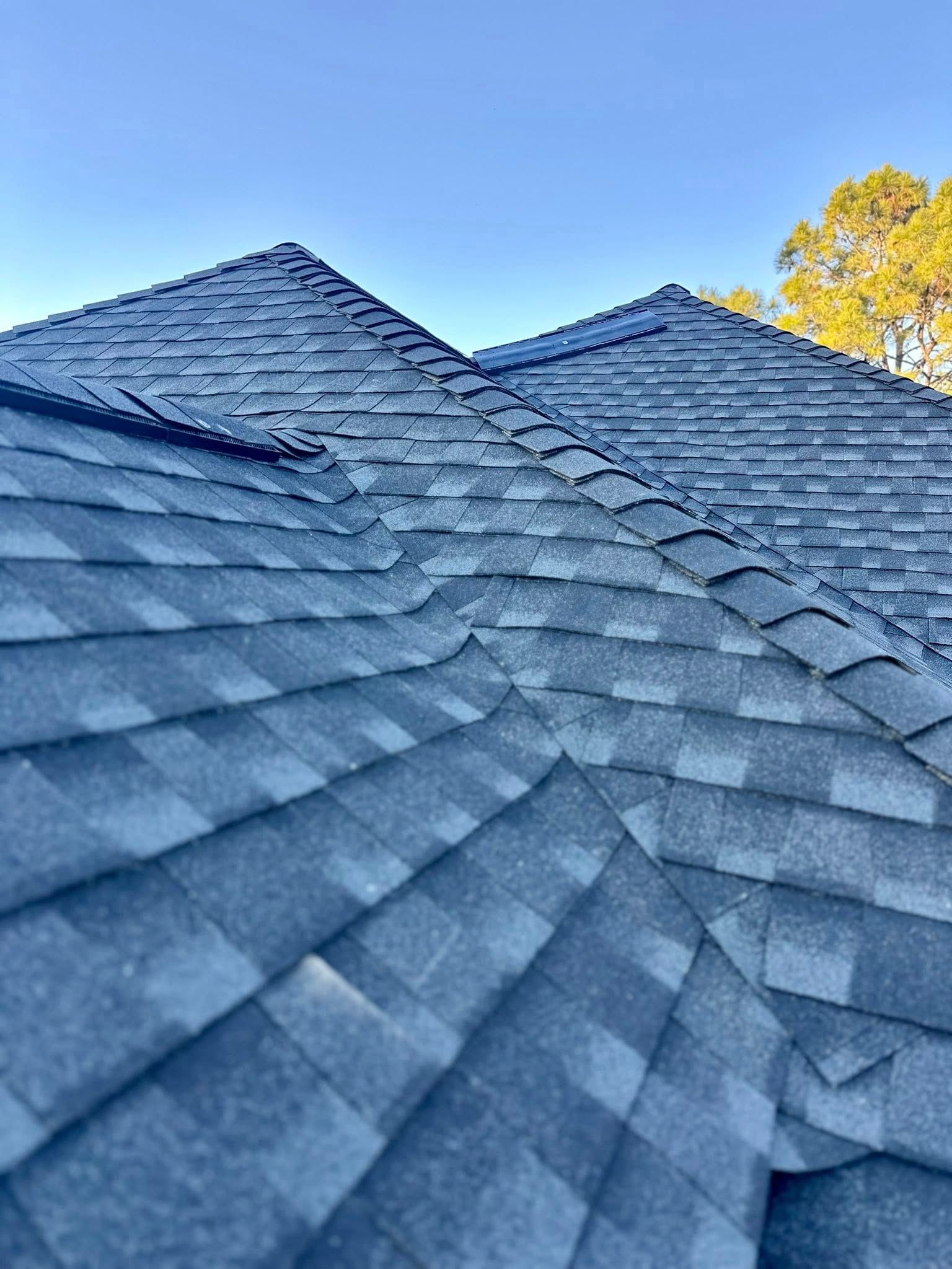 Low-angle view of gray architectural asphalt roof shingles against a clear blue sky.