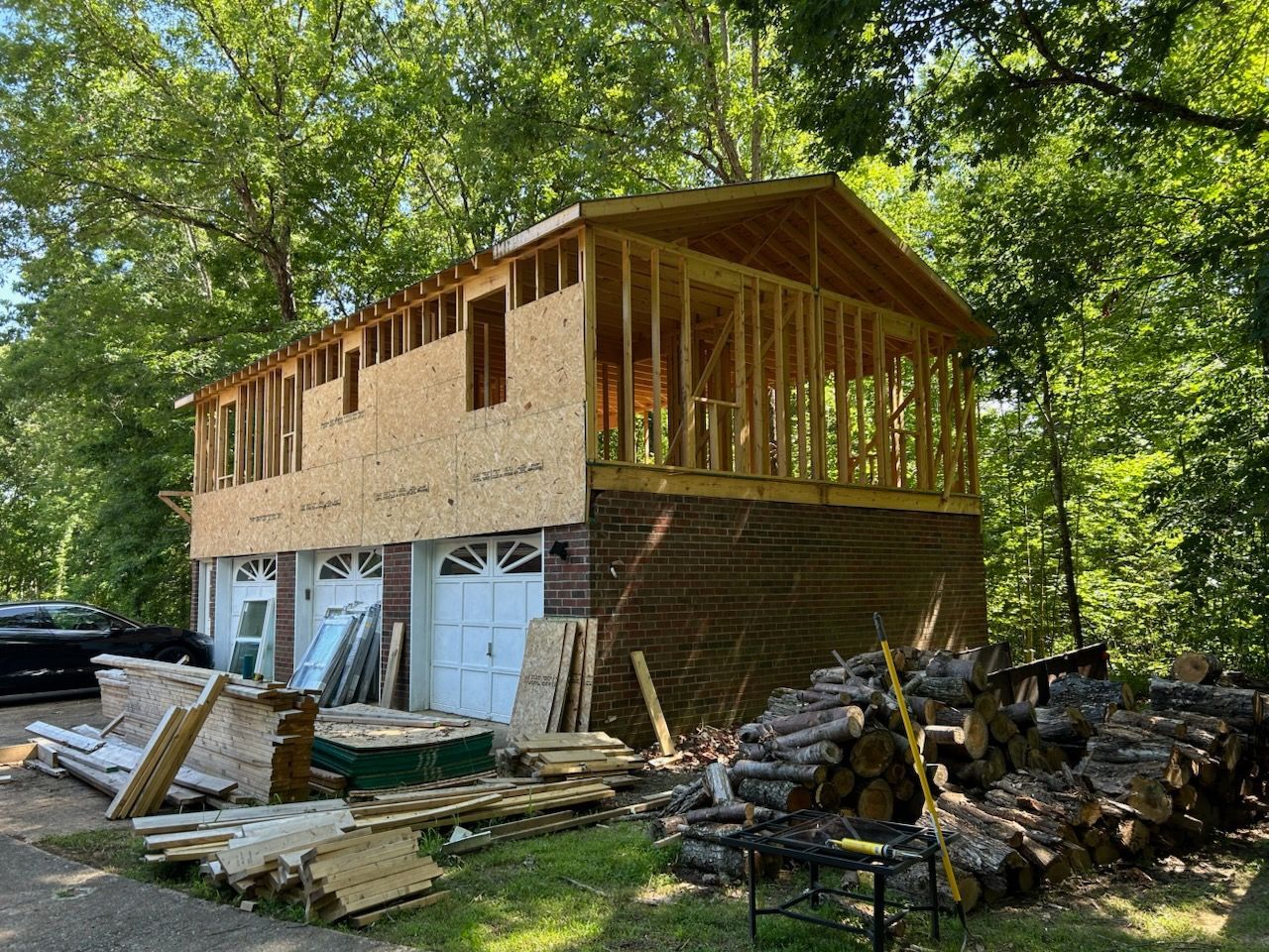 Construction of a two-story building with brick garage and wooden framing for upper level; surrounded by trees.