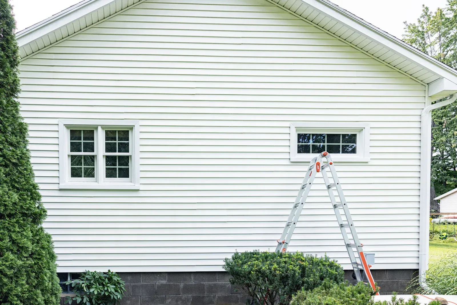A ladder is sitting on the side of a white house.