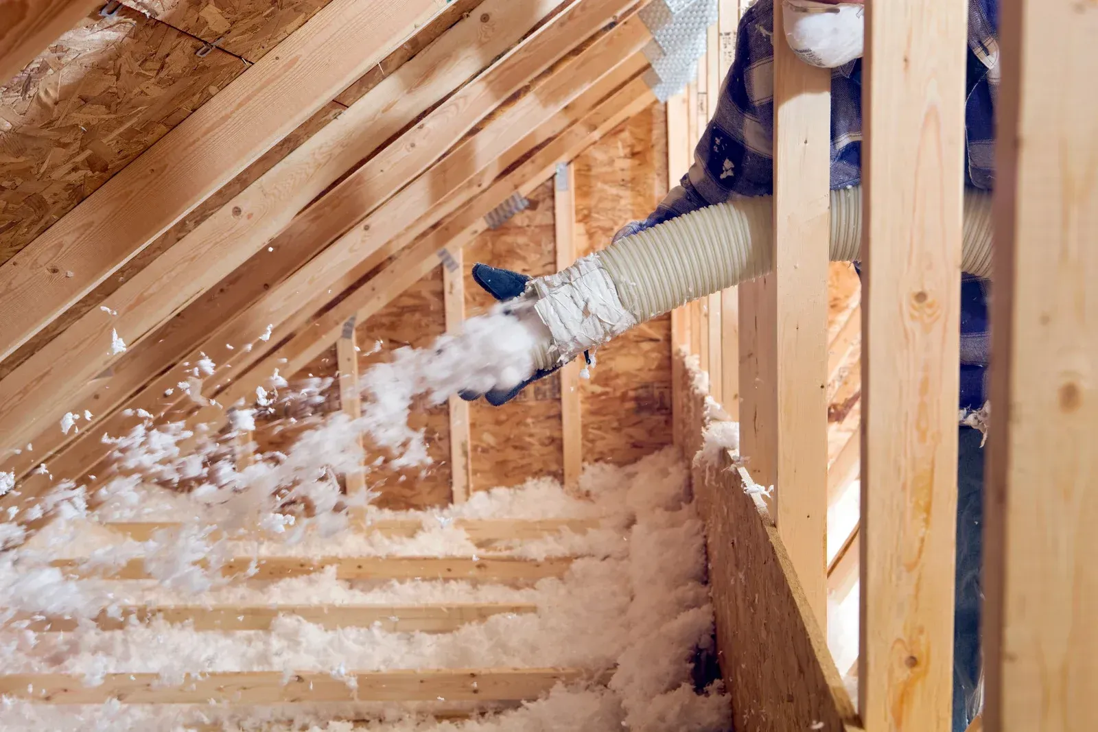 A person is blowing insulation into the attic of a house under construction.