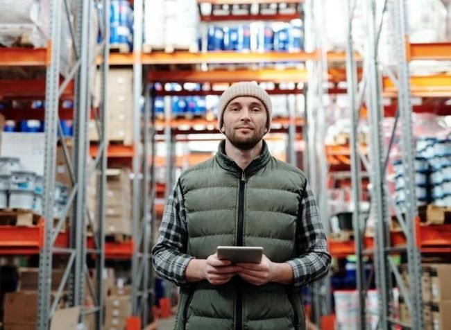 A man is standing in a warehouse holding a tablet.