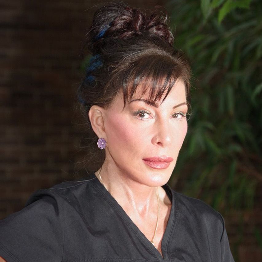 A woman wearing a black scrub top and purple earrings is standing in front of a brick wall .Kara Newman