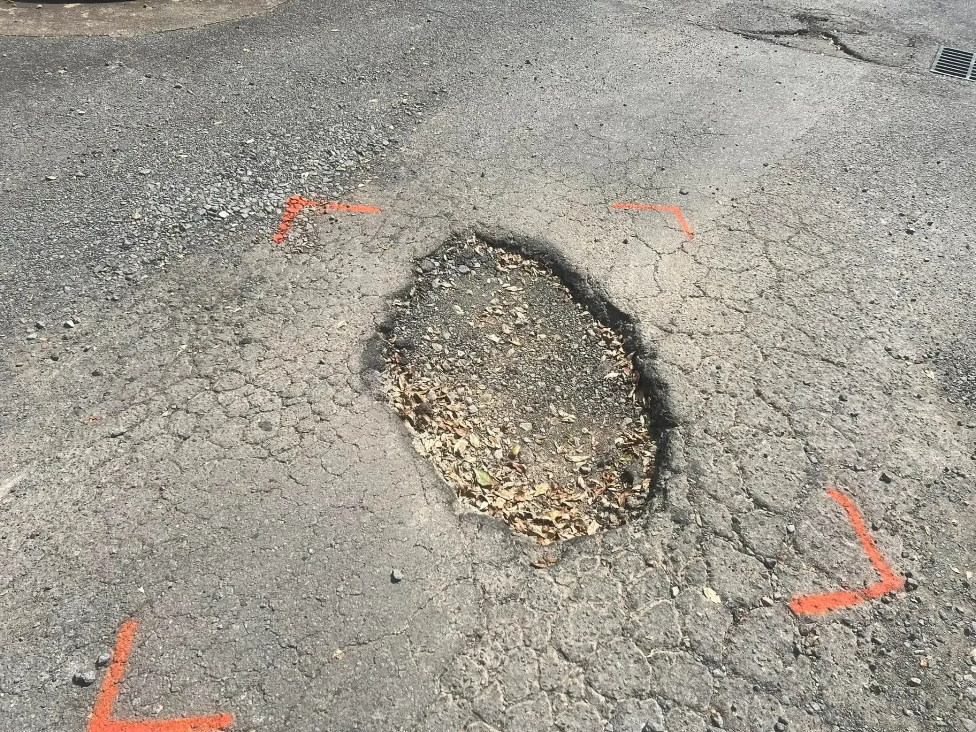 Pothole in asphalt road, marked by orange paint.