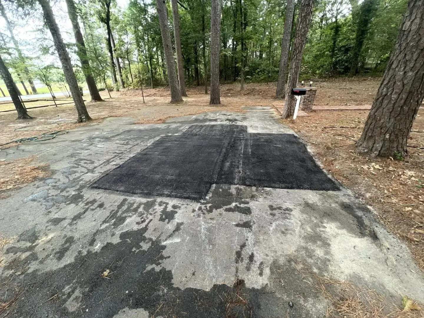 Asphalt campsite with two black mats, surrounded by trees.
