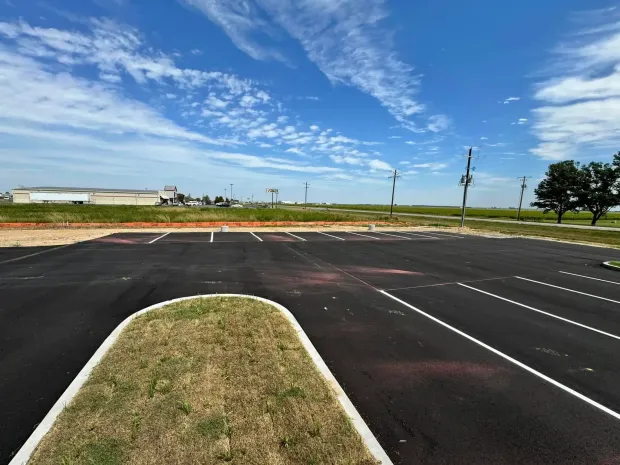 Empty asphalt parking lot with white lines, grass divider, and blue sky.