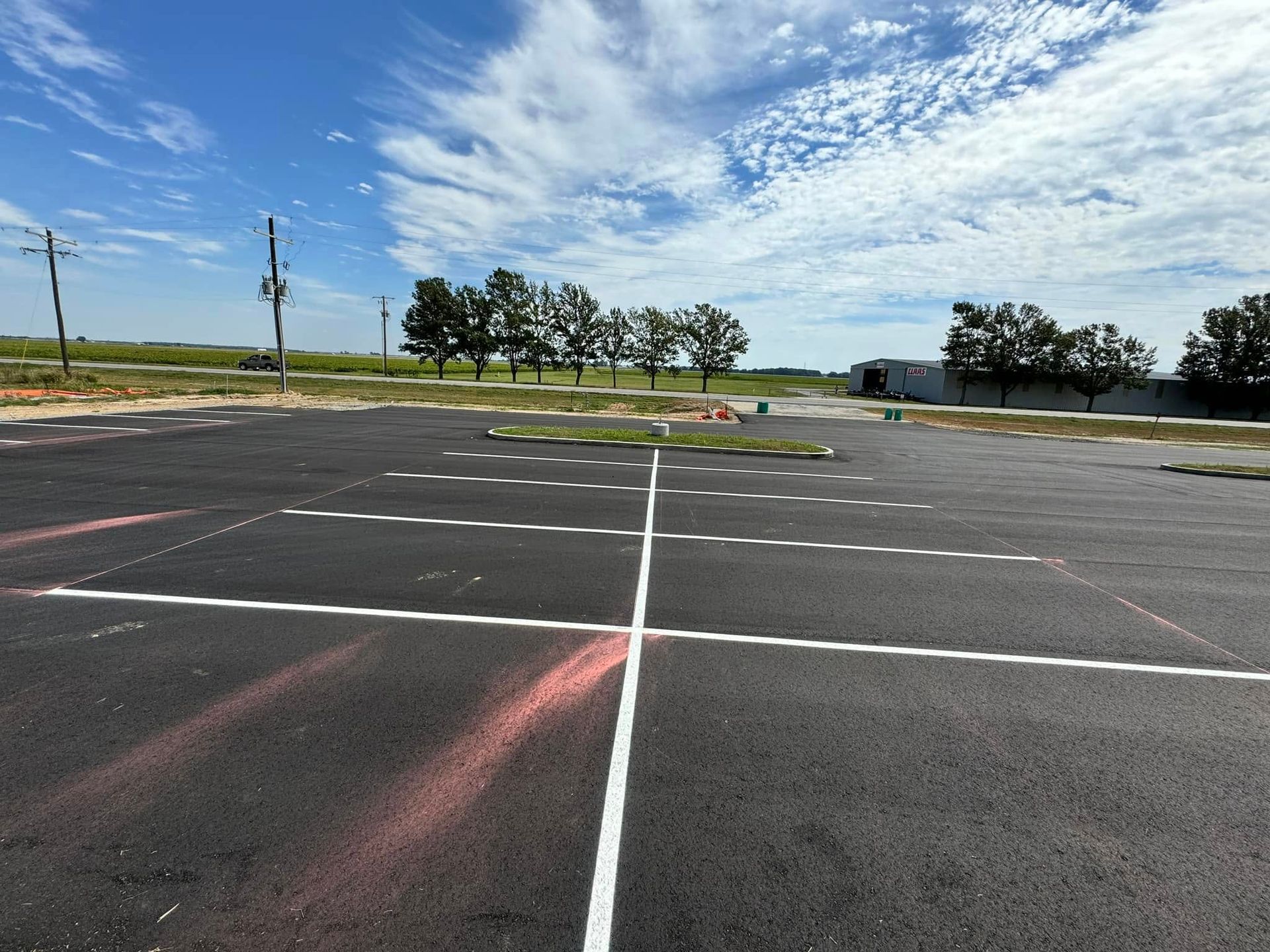 Newly paved parking lot with white lines and spray-painted red markings, under a blue sky.