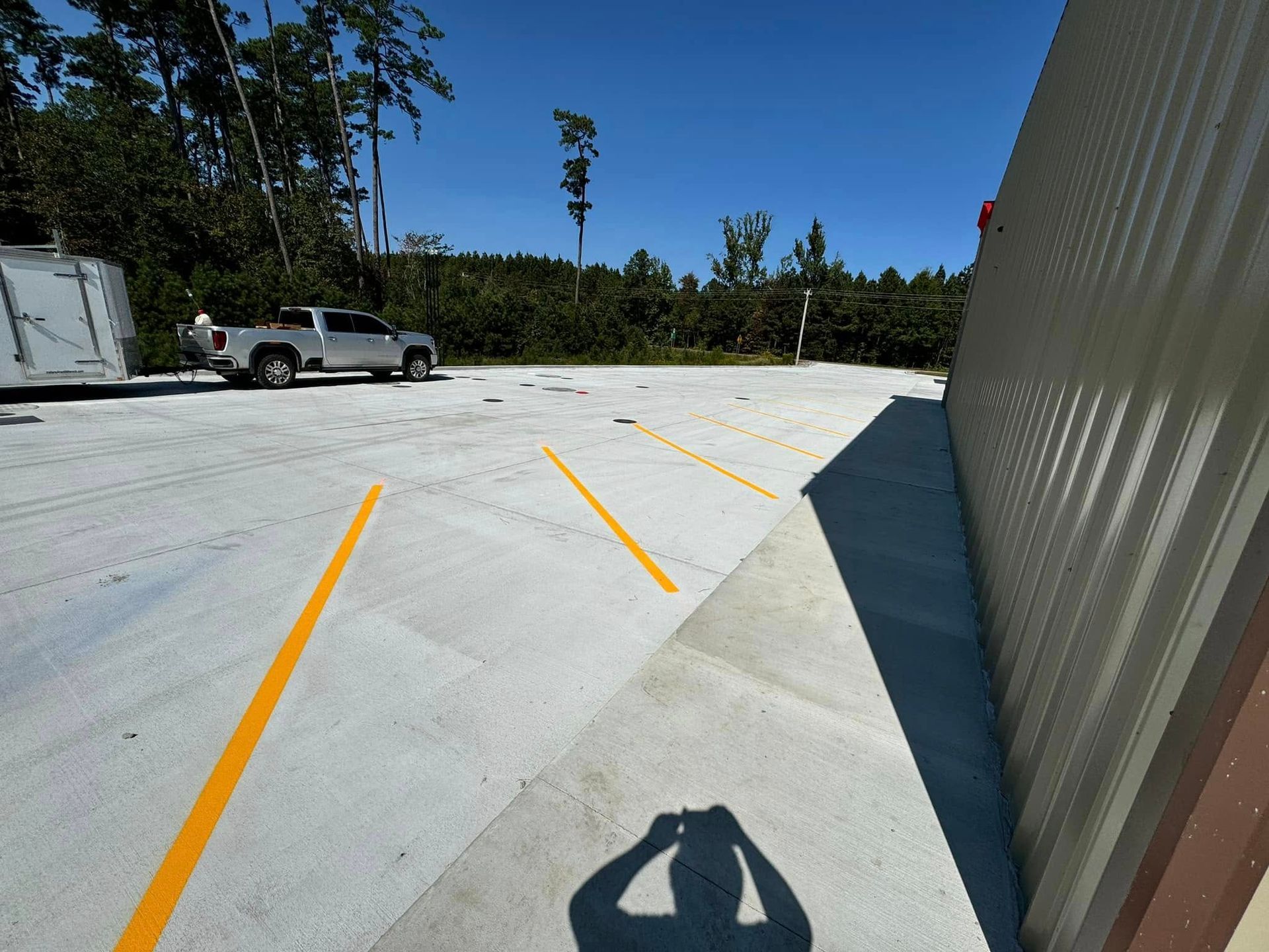 A silver truck parked in a concrete parking lot with yellow lines. Shadow of a person taking photo.
