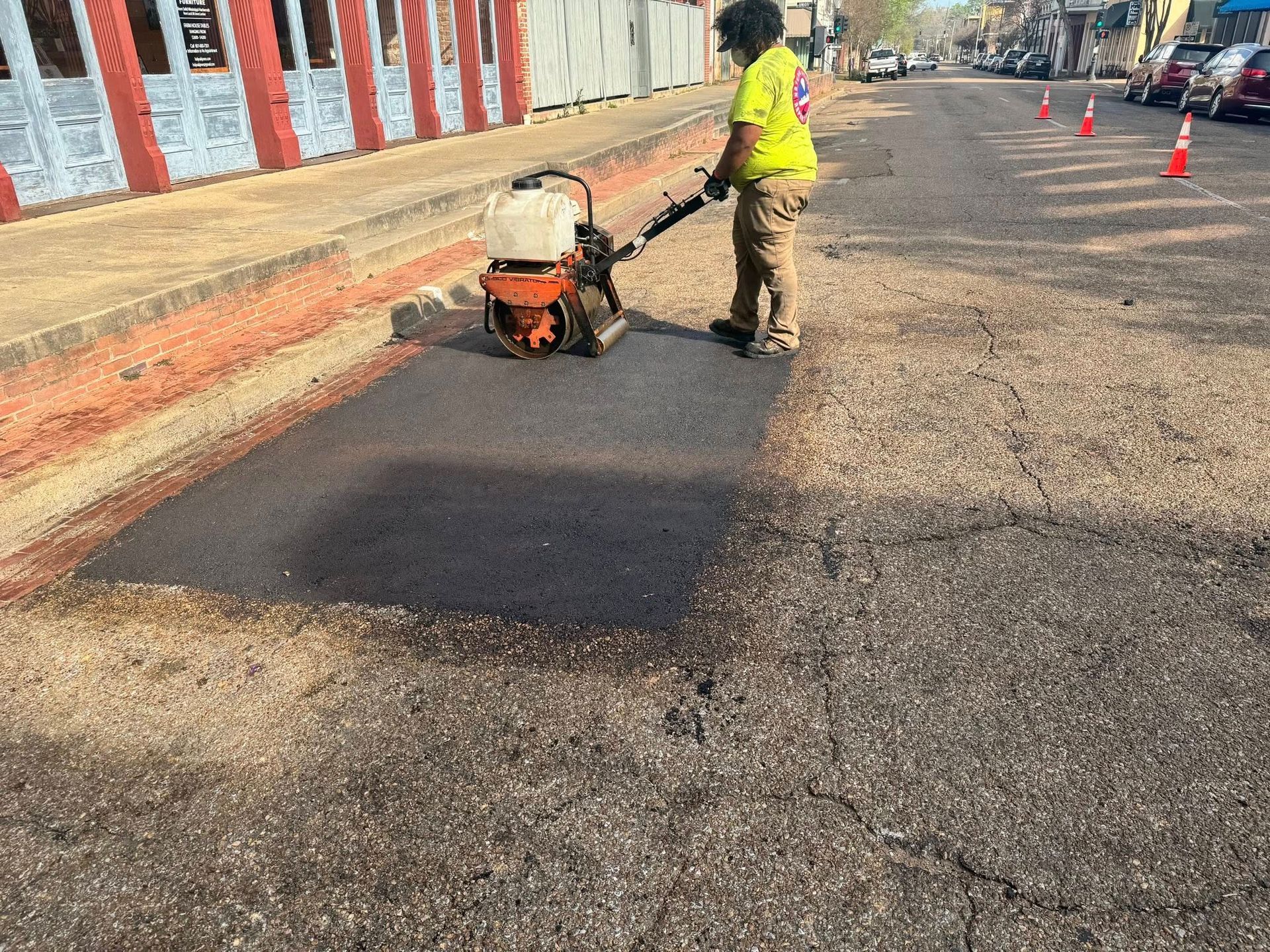 Road worker compacting fresh asphalt on a city street with an orange compactor.