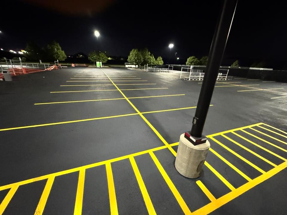 Empty parking lot at night, with yellow painted lines on the dark asphalt. Street light pole in foreground.