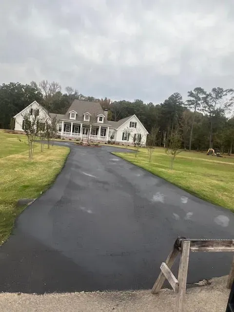 Large white house with a long, dark driveway on a cloudy day. Green grass surrounds the house.