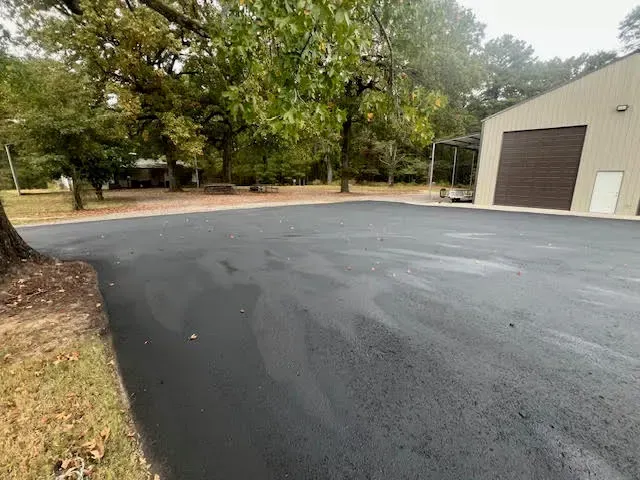 Newly paved black asphalt driveway next to a building with a large garage door.